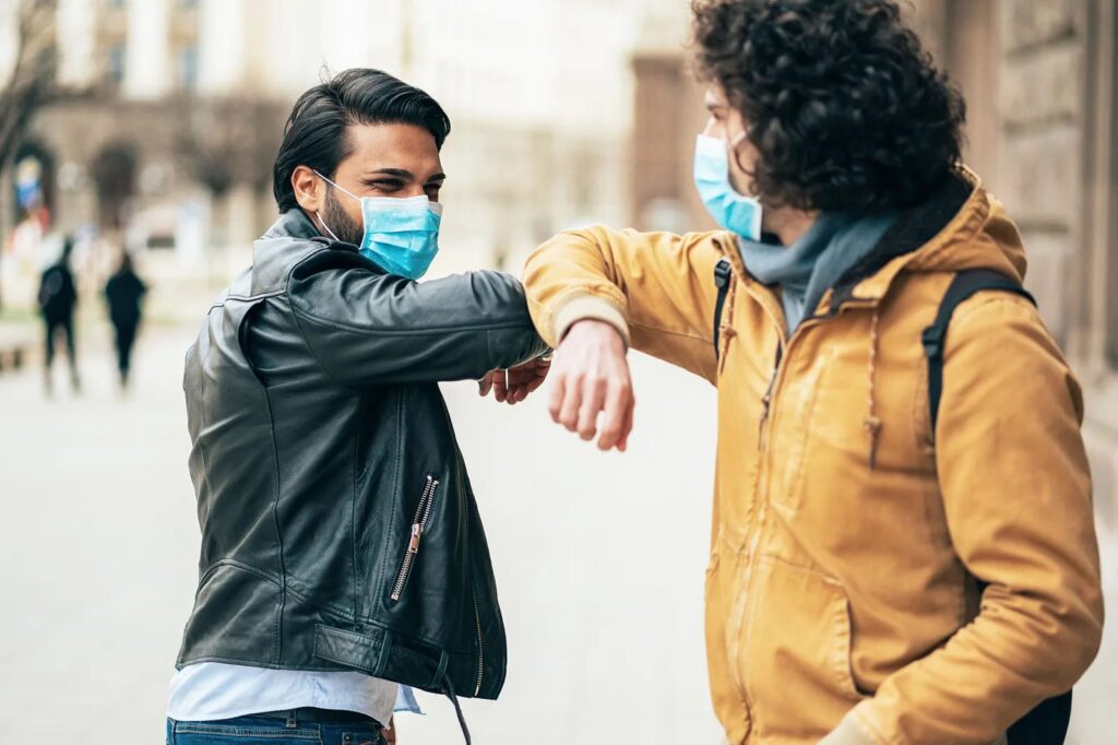 Two people wearing masks, greeting by touching elbows